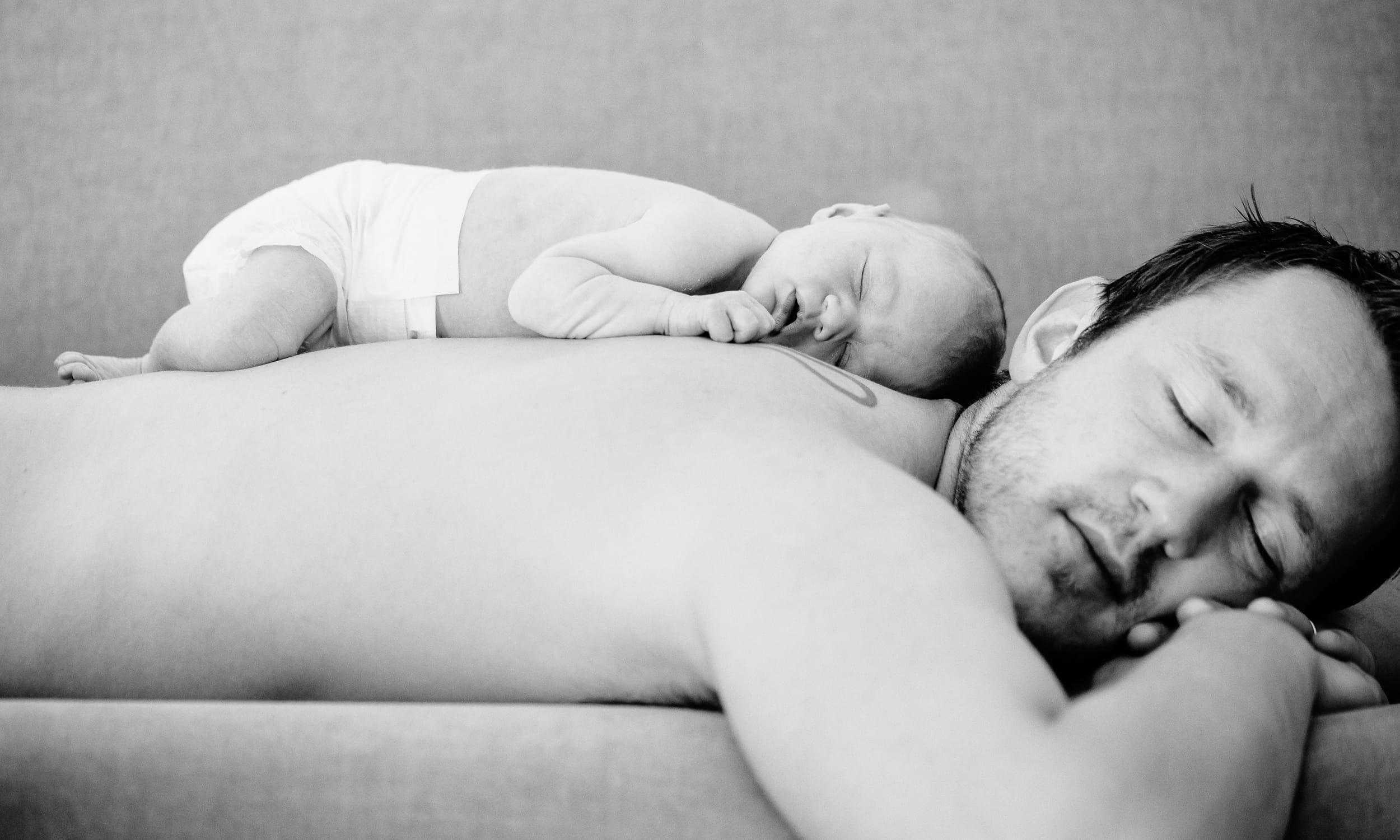 Baby liegt auf Rücken vom Vater. Beide schlafen.