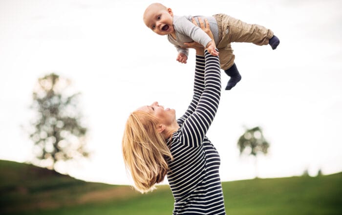 Mutter hält Baby hoch in die Luft und beide lachen