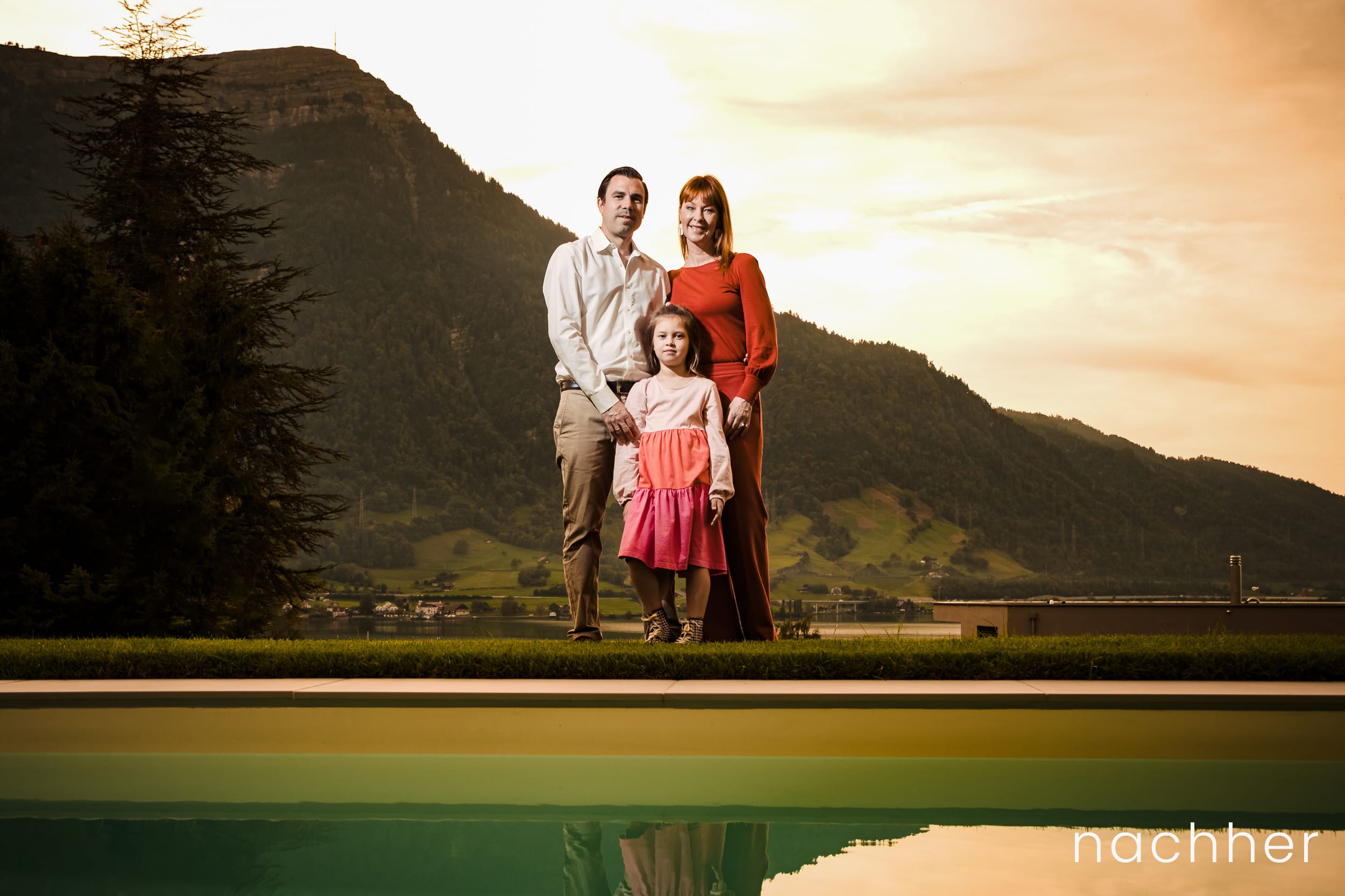 Familie steht hinter Pool mit Spiegelung und Sonnenuntergang hinter der Rigi.